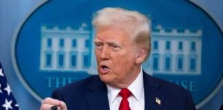 A man in a suit speaking at a press conference with a serious expression