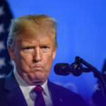 Trump’s Housing Bombshell Stuns Critics Man speaking at podium with microphones and flags