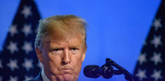Man speaking at podium with microphones and flags