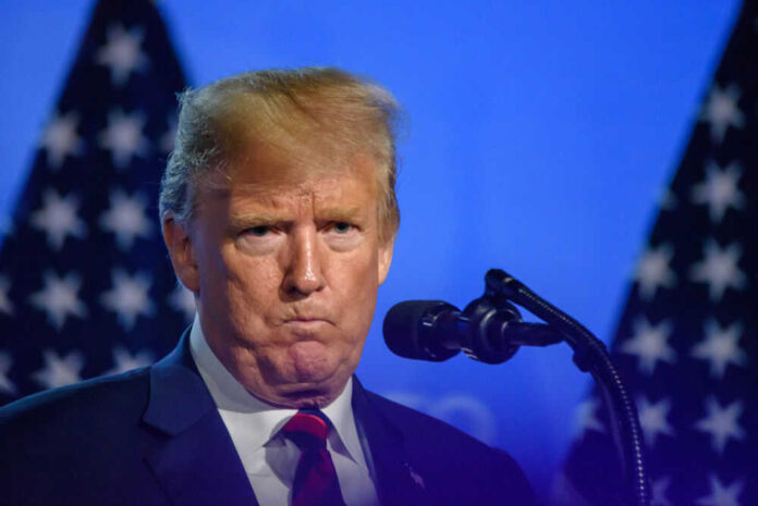 Man speaking at podium with microphones and flags