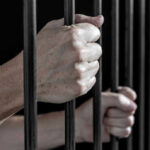 Hands gripping prison cell bars tightly