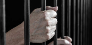 Hands gripping prison cell bars tightly