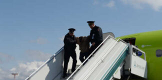 Police officers escorting a passenger down the stairs from an airplane