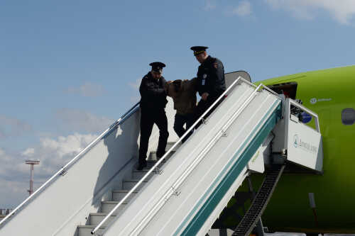 shutterstock_1503093863.jpg Police officers escorting a passenger down the stairs from an airplane