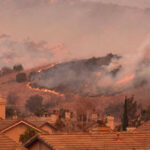Wildfire approaching residential area with smoke rising