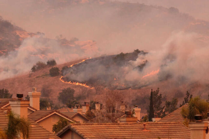 Wildfire approaching residential area with smoke rising